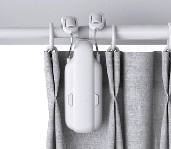 Smart curtain motor device attached to curtain rod with gray curtains, home automation