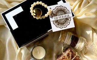Eid Mubarak gift set with pearl bracelet, macarons, brownies, and candle on golden fabric