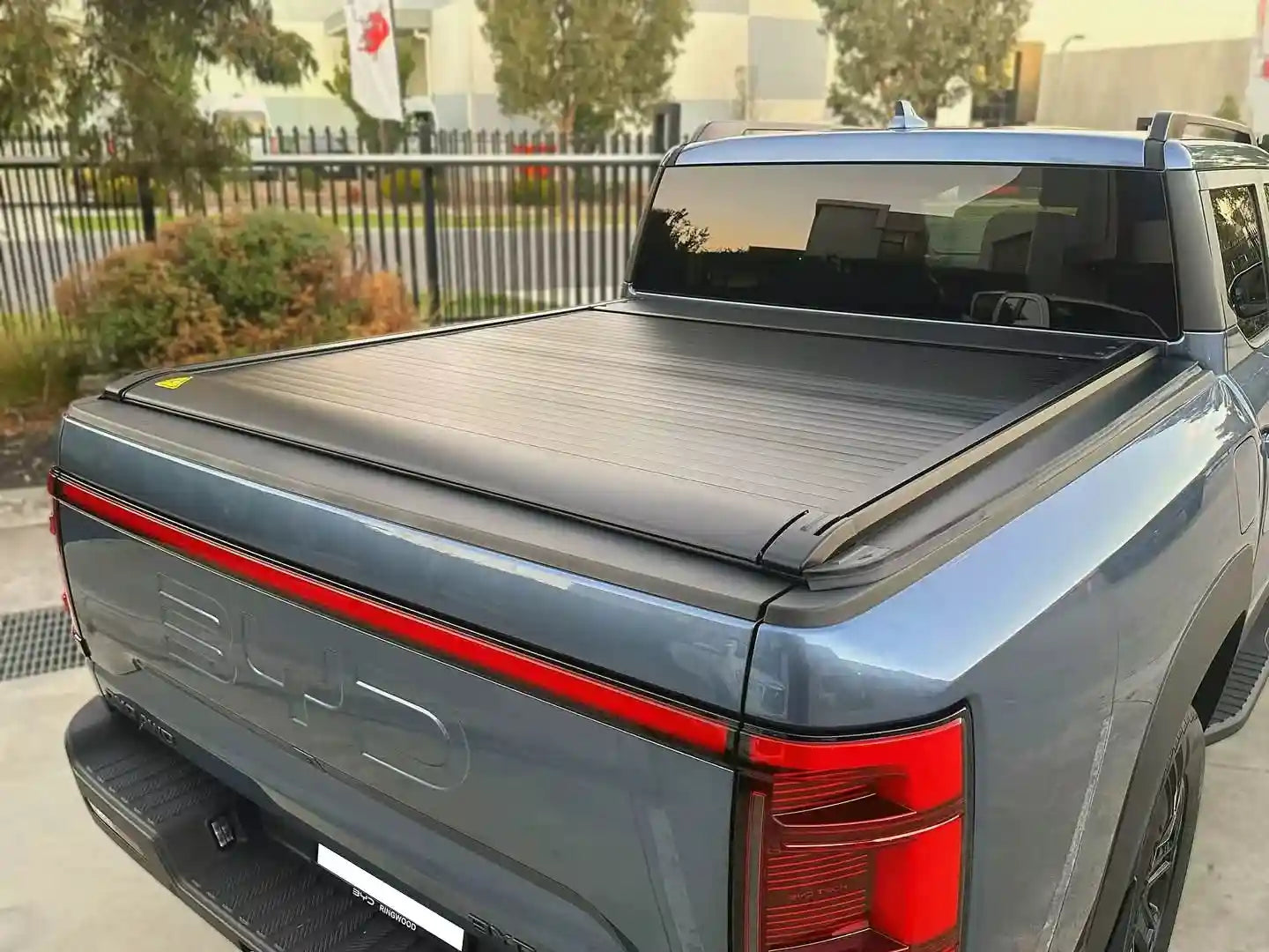Gray BYD pickup truck with black roll-up tonneau cover, rear view in outdoor setting