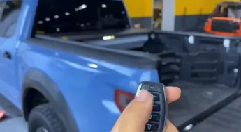 Hand holding car key fob near blue pickup truck in garage